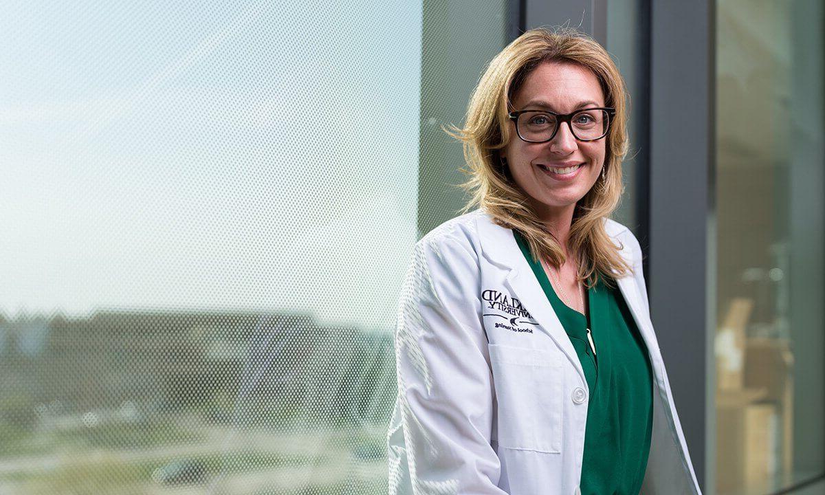 A woman in a lab coat smiles at the camera.